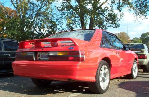 1998 Ford Crown Victoria - The rear view of a red Ford Mustang shows its distinctive taillights and spoiler, with another vehicle visible to the right.
