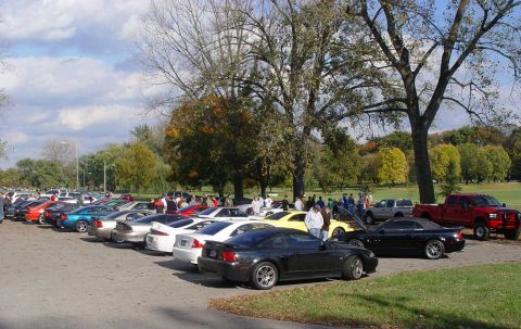 1998 Ford Crown Victoria - Outdoor car meet with numerous vehicles and attendees gathered under a partly cloudy sky.