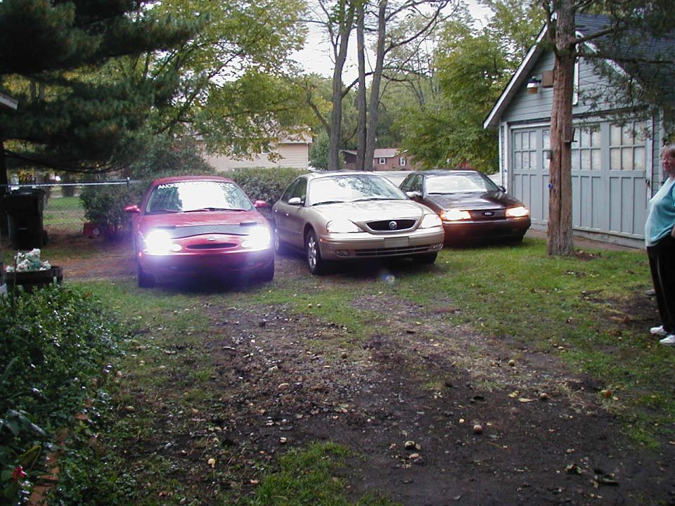 red sedan, gold sedan, and brown sedan parked in a driveway near a garage