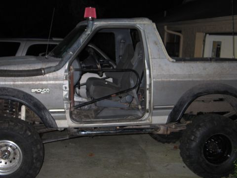 1992 Ford Bronco - Night shot of a silver 1990s full-size Ford Bronco stripped for trail use, doors and top removed, internal roll cage and tube rocker slider…