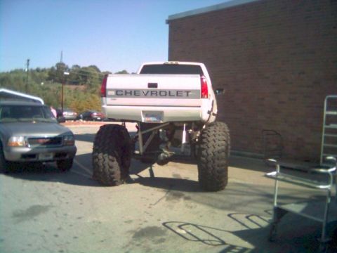 1984 Ford Bronco II - A heavily modified Chevrolet pickup truck with massive tires is parked next to a silver SUV.