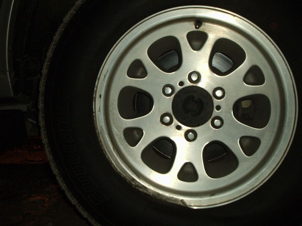 Close-up of a silver multi-spoke wheel with a black tire. "SUPERMOTORS.NET" text visible