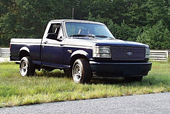 Dark blue Ford F-150 pickup truck parked on grass, front 3/4 view
