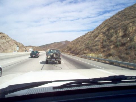 1988 Ford Bronco - A 1988 Ford Bronco is seen from behind on a highway, with a spare tire attached to its tailgate. Another vehicle is visible ahead.