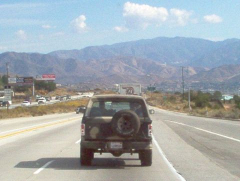 1988 Ford Bronco - A 1988 Ford Bronco is seen from behind while driving on a highway with mountains in the background.
