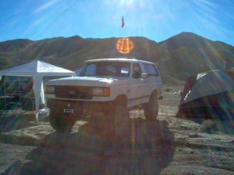 1988 Ford Bronco - A white 1988 Ford Bronco is parked in a desert campsite with tents and mountains in the background.