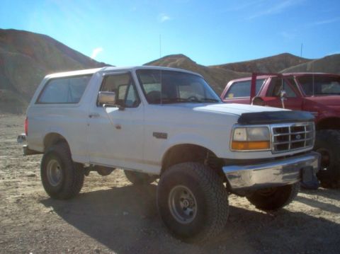 1988 Ford Bronco - A white Ford Bronco is parked in a dusty, outdoor area with hills in the background and another vehicle nearby.