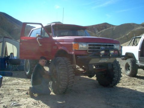 1988 Ford Bronco - A modified red Ford Bronco sits in a desert landscape next to another vehicle.