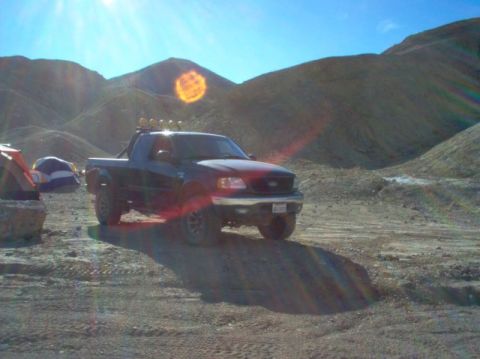1988 Ford Bronco - This black pickup truck, likely from the late 1990s, is parked in a dry, hilly terrain with tents nearby.