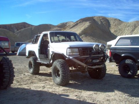 1988 Ford Bronco - Modified SUV with off-road tires and accessories sits in a dry, mountainous terrain under a clear blue sky.