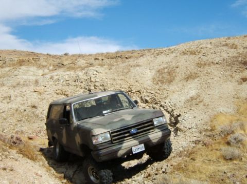 1988 Ford Bronco - A Ford Bronco navigates a steep, rocky incline under a blue sky.