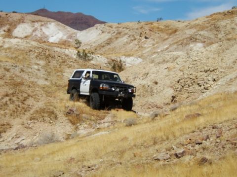 1988 Ford Bronco - A modified Ford Bronco navigates a challenging off-road terrain under a clear blue sky.