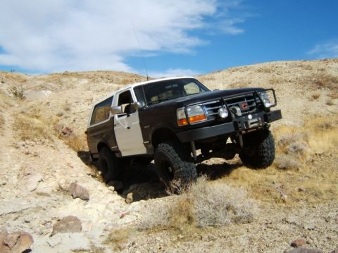 1988 Ford Bronco - A modified Ford Bronco navigates a challenging off-road trail under a clear blue sky.