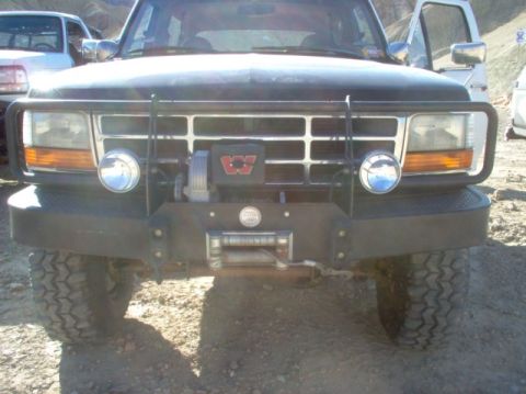 1988 Ford Bronco - Front view of a black Ford Bronco with a winch and brush guard, parked next to a white truck.