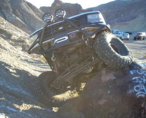 1988 Ford Bronco - This heavily modified Ford Bronco is navigating a challenging rocky terrain, with other vehicles visible in the distance.