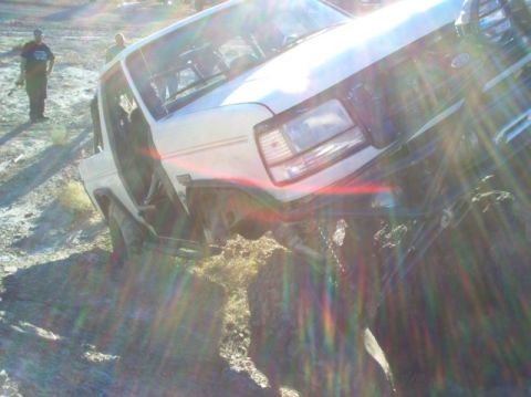 1988 Ford Bronco - A white 1988 Ford Bronco is shown tilted on its side on a dirt embankment with the driver's door open.