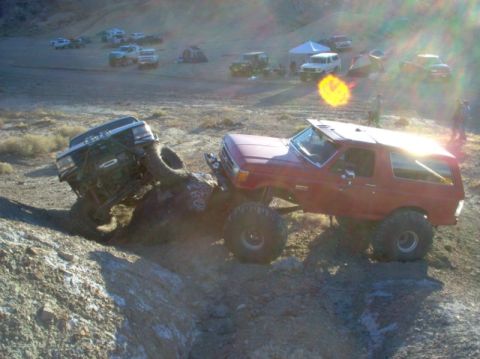 1988 Ford Bronco - Two modified trucks tackle a challenging off-road obstacle in a desert landscape.