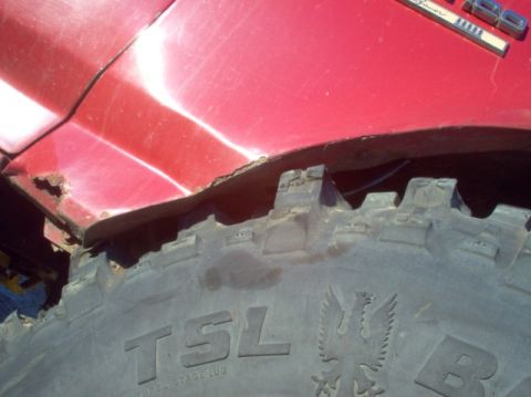 1988 Ford Bronco - Close-up of a red fender and tire on a 1988 Ford Bronco, showing rust and damage.