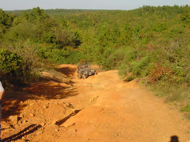Jeep on an orange-dirt descent overlooking rolling forested hills under blue sky