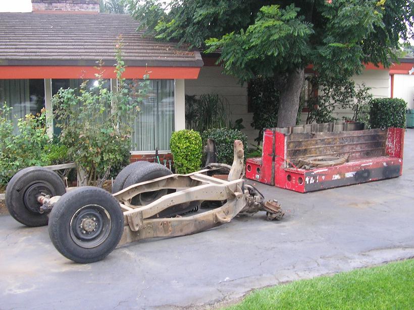 Truck chassis with wheels and a separate red truck bed on pavement