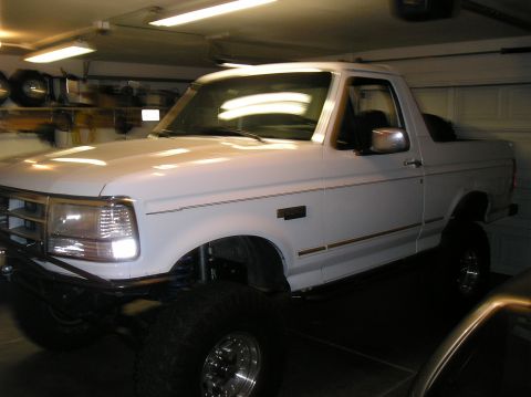 1993 Ford Bronco - This lifted white Ford Bronco is parked in a garage with overhead lighting.