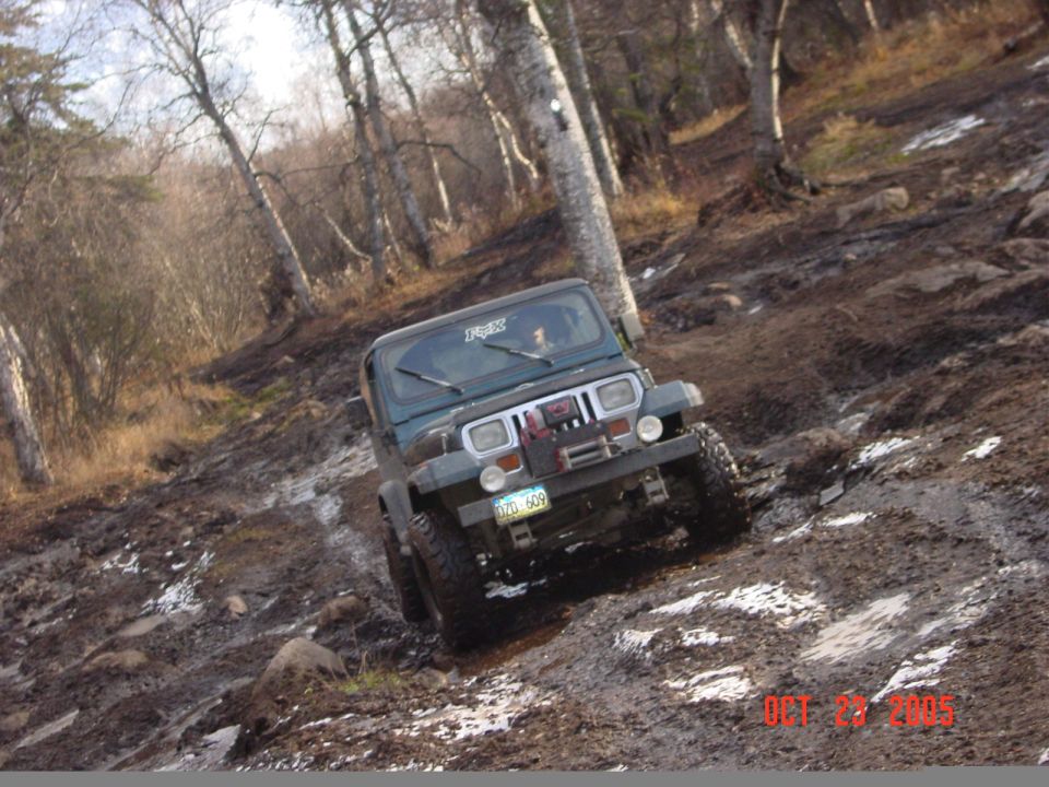 1995 Jeep YJ climbing a steep, muddy, wooded trail. License plate reads GZG 609