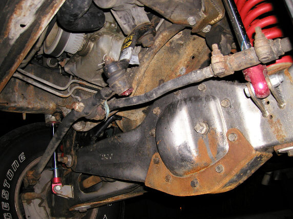 Underside of front solid axle with rusty differential, steering linkage, red coil spring and Bridgestone tire