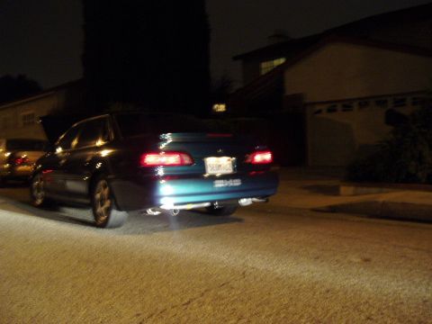 1993 Ford Taurus - A blue sedan with its exhaust pipes visible is parked on a street at night.