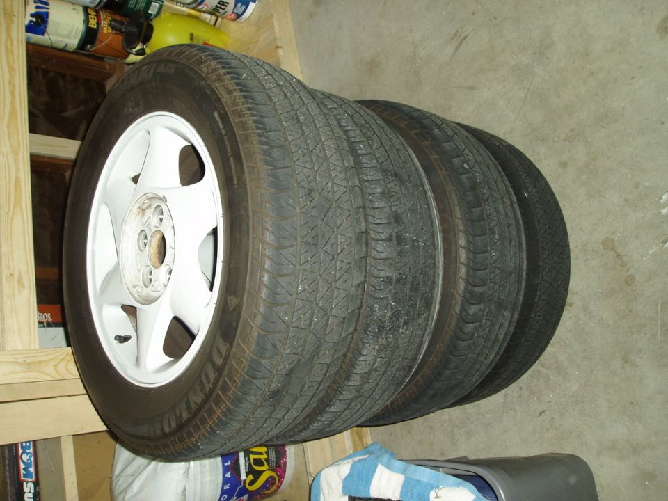 Four mounted tires on white five-spoke alloy wheels stacked on a garage floor