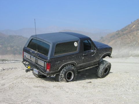 1985 Ford Bronco - This modified Ford Bronco is shown off-roading on a dusty, hilly terrain.