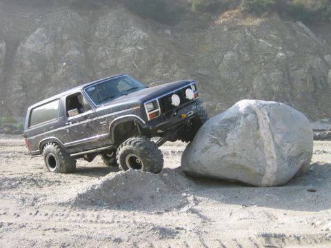 1985 Ford Bronco - A modified Ford Bronco navigates a large boulder on a rocky, off-road trail.