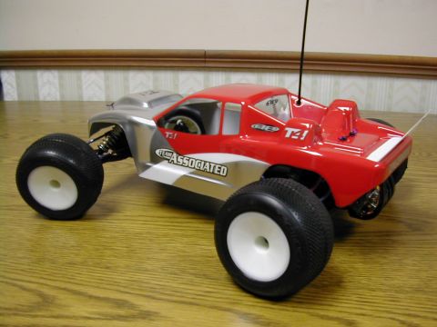 1994 Ford Bronco - A red and silver remote control monster truck, likely a Team Associated model, is shown from a 3/4 front view on a wooden surface.