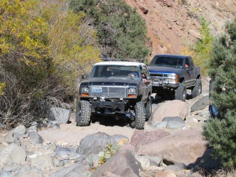 1986 Ford Bronco - Two off-road vehicles navigate a challenging rocky path through a dry, mountainous landscape.