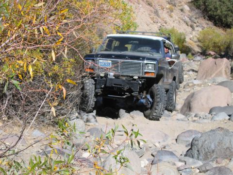 1986 Ford Bronco - Ford Bronco tackling a challenging off-road course with large rocks and sparse vegetation.
