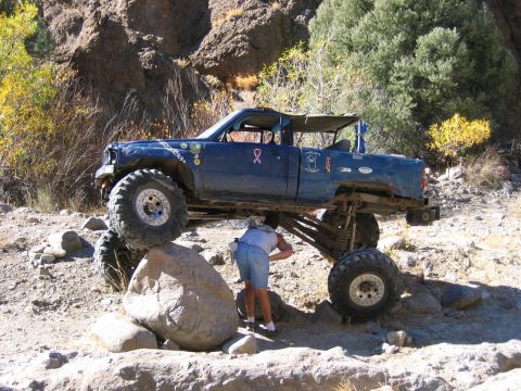 1986 Ford Bronco - A modified blue truck navigates a challenging rocky path with a person inspecting its undercarriage.