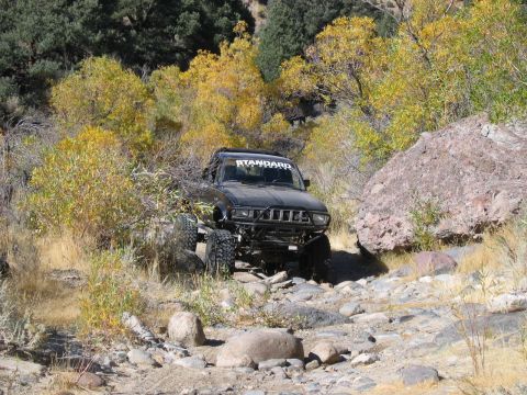 1986 Ford Bronco - A modified black SUV navigates a rocky off-road trail surrounded by autumn foliage.