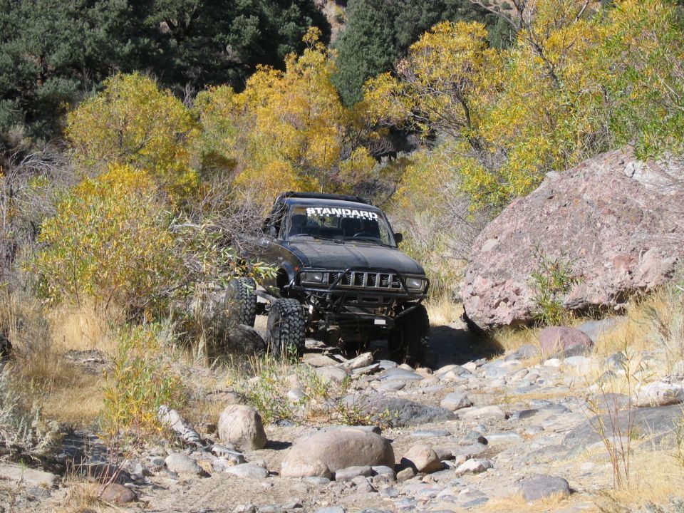 Black off-road SUV with large tires on a rocky trail, "STANDARD" banner on windshield