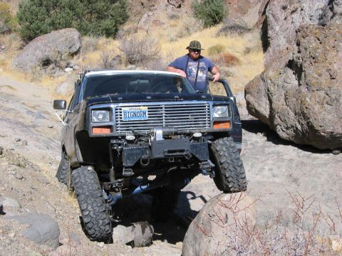 1986 Ford Bronco - This modified SUV is tackling a challenging rocky path, demonstrating its off-road capabilities.