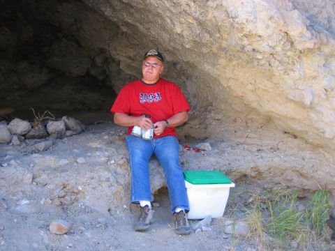 1986 Ford Bronco - A man takes a break inside a cave, holding cans and sitting next to a cooler.