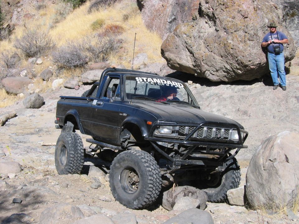 Black off-road pickup truck with large tires and a roll bar, driving on a rocky terrain