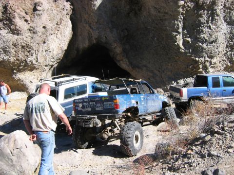 1986 Ford Bronco - Multiple off-road vehicles navigate a rocky canyon trail, including a heavily modified blue Toyota pickup.