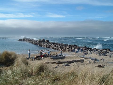 2000 Ford F-250 - People enjoy a day at the beach near a rocky jetty with waves crashing in the background.