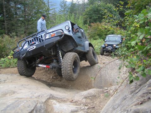1990 Ford Bronco - Two Jeep Wranglers navigate a challenging rocky trail in a wooded area.