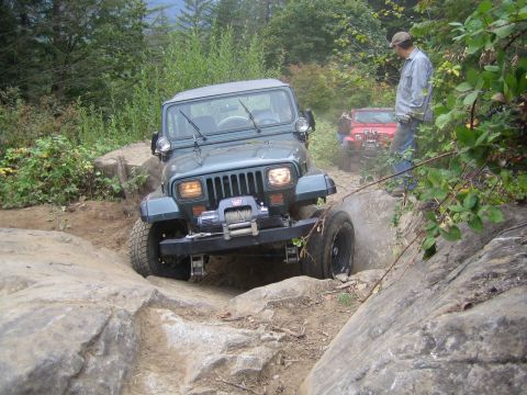 1990 Ford Bronco - A gray Jeep Wrangler tackles a challenging rocky trail, with another Jeep visible behind it.