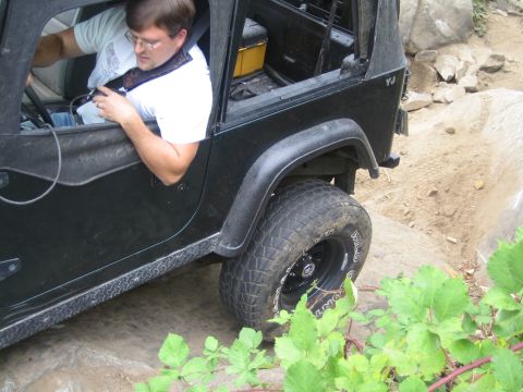1990 Ford Bronco - A black Jeep Wrangler YJ navigates a rocky trail with a driver inside.
