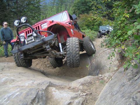 1990 Ford Bronco - A red Jeep Wrangler navigates a difficult rocky trail, with another Jeep visible further up the path.