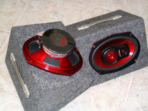 1991 Ford Crown Victoria LTD - Two red car stereo speakers are mounted in a grey carpeted enclosure, with visible text on one speaker indicating '3 WAY AUDIO SPEAKERS'.