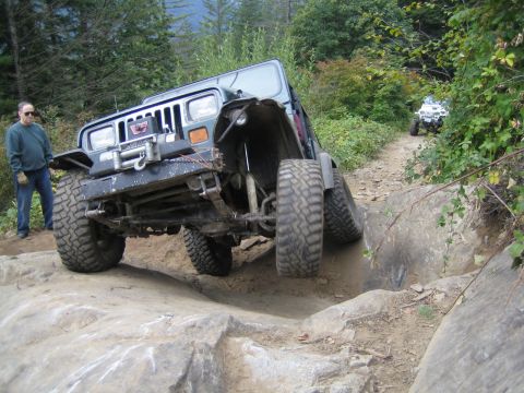 1990 Ford Bronco - A modified Jeep Wrangler tackles a challenging off-road course, with another vehicle in the distance.