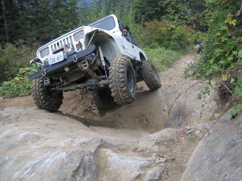 1990 Ford Bronco - A modified Jeep Wrangler navigates a challenging rocky terrain on an off-road trail.
