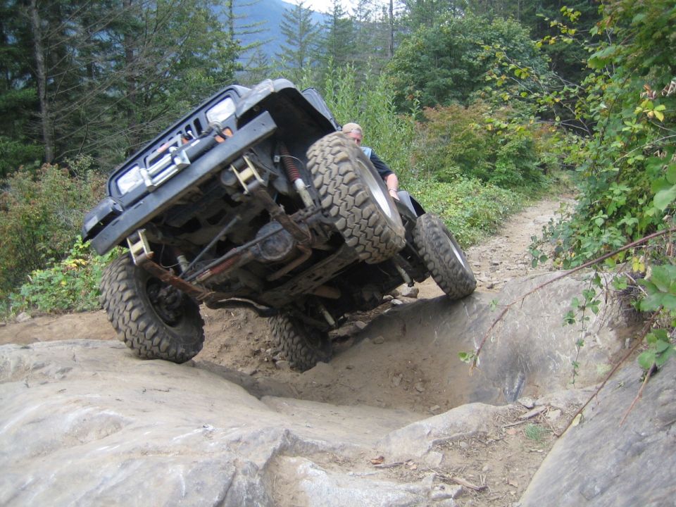 Black off-road vehicle tilted on rocks, underside visible, driver in seat